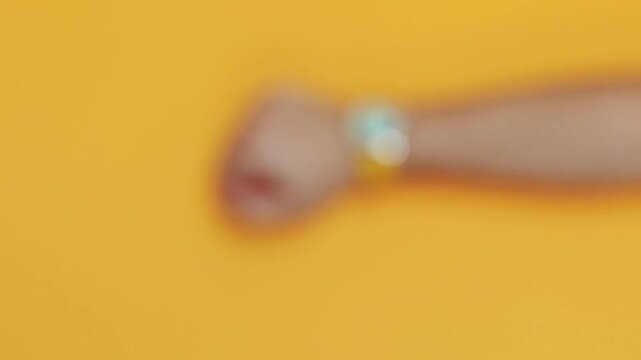 Man's arm wearing a wristwatch with a turquoise dial and yellow strap against a yellow background. Concept of dopamine dressing fashion