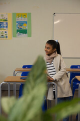 Obraz premium African American schoolgirl standing by wooden desks in classroom near potted plant, copy space