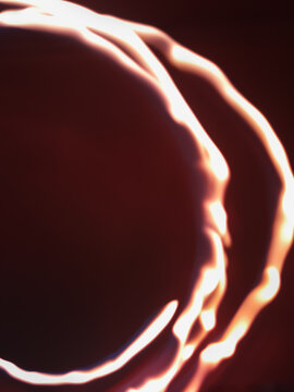 A long-exposure effect or light painting technique featuring curved white-and-orange trails of firelight against a dark background.