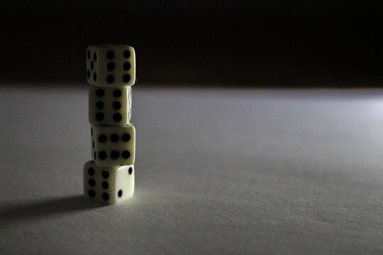 Four stacked white dice with black dots cast shadows on a white surface
