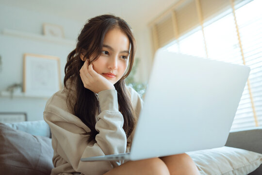 Young woman using laptop while sitting on bed at home, online communication, remote work and digital lifestyle