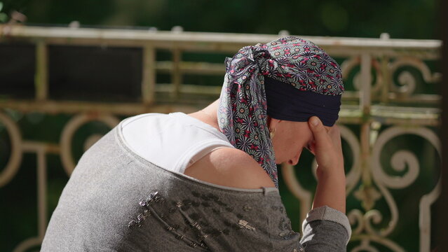 Woman undergoing chemotherapy sitting on balcony with head in hand, contemplative moment reflecting emotional burden, resilience, uncertainty and personal recovery journey