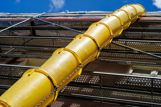 Yellow plastic debris chute on construction scaffolding against blue sky. Low angle view of building renovation site.