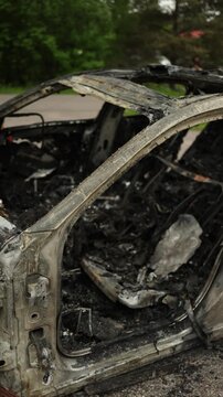 Vertical screen burned out automobile after a devastating traffic accident showing severe fire damage blackened surfaces and destroyed components as a stark road safety scene