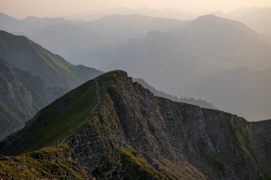 Dramatic rocky mountain crest overlooking hazy layered peaks in the Swiss Alps at warm morning light.