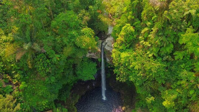 Aerial view of Curug Telu waterfall surrounded by dense tropical rainforest and lush green foliage in Baturaden, Jawa Tengah, Indonesia.