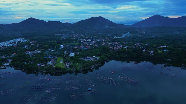 Slow pan drone footage across Sampaloc Lake Fish ponds Mount San Cristobal showcasing San Pablo City's urban landscape, tropical forests , and peaceful twilight atmosphere.