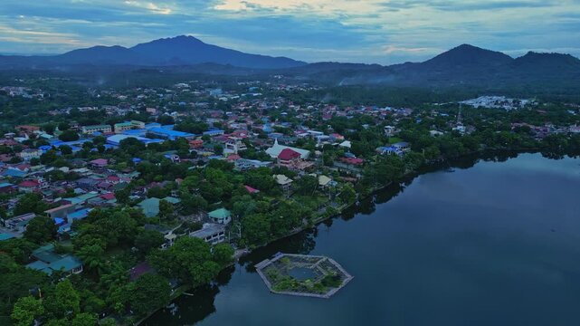 Slow pan drone footage across the Sampaloc Lake district featuring Iglesia Ni Cristo San Pablo City, Laguna, Philippines the surrounding community, and Mount San Cristobal.
