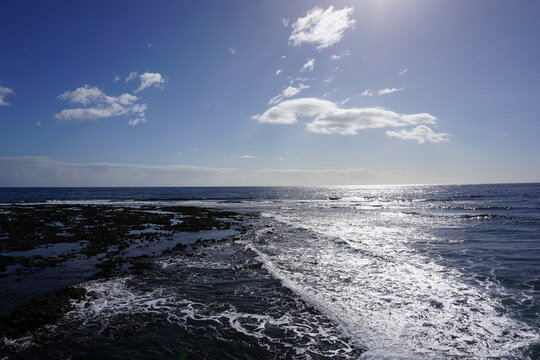 Sunlight sparkling on the sea beside a rocky volcanic shore