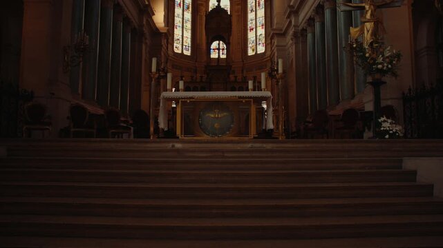 Historic church altar area viewed beyond wooden steps and seating with ornate religious architecture in warm low light