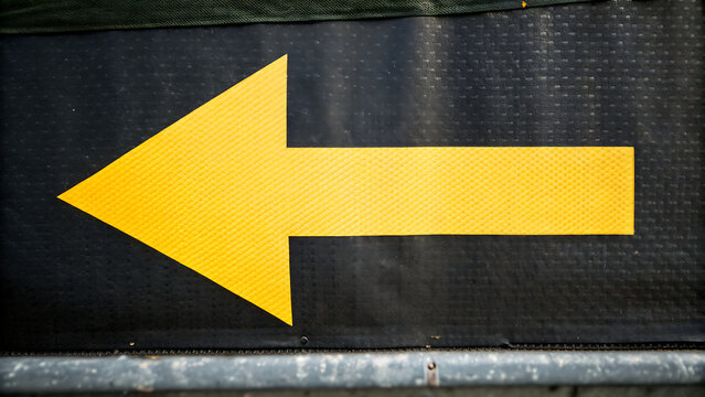 Bright yellow right turn arrow sign on dark textured wall for navigation and direction guidance