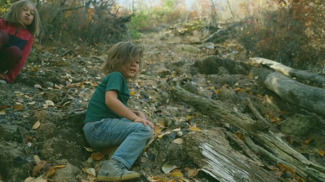 Two boys sitting together on rocky ground near a creek in autumn woods