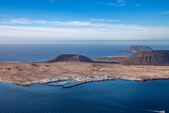 Panoramic view of La Graciosa Island from a high viewpoint in Lanzarote, Canary Islands, Spain. The landscape shows the volcanic island surrounded by the deep blue waters of the Atlantic Ocean, with i