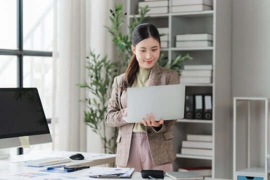 Focused Professional: A diligent businesswoman stands at her desk, intently focused on her laptop, surrounded by the organized clutter of a modern office.