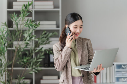 Businesswoman in Office: A focused businesswoman, dressed in professional attire, engages in a phone conversation while holding a laptop in a modern office setting.