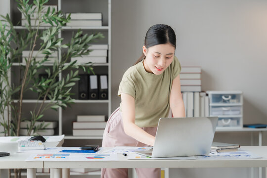 Focused Professional Working on Laptop: A young woman diligently works on her laptop at a well-organized desk, surrounded by office supplies and bookshelves.