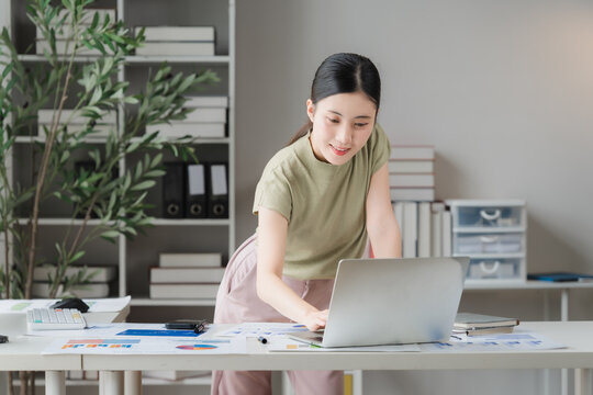 Focused Professional: A young woman works diligently on her laptop at a modern desk, surrounded by organized shelves and plants, embodying productivity and modern workspace aesthetics.