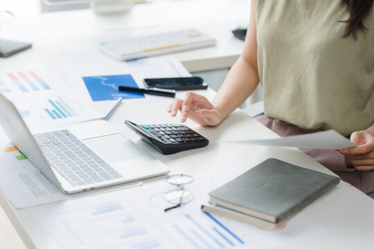 Financial Planning Desktop: A person's hands are seen using a calculator and laptop amidst a desk filled with financial documents, charts, and notebooks, symbolizing financial planning and analysis.