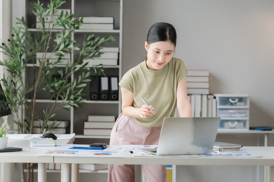 Focused Professional at Work: A young woman, focused and determined, works diligently at her laptop in a well-organized home office, surrounded by plants and books.