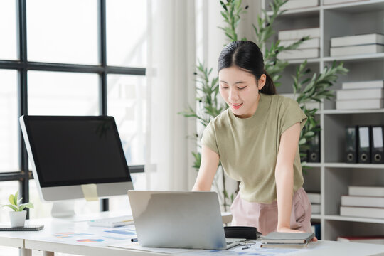 Focused Professional: A young woman diligently works at her desk, illuminated by natural light, surrounded by office essentials, embodying productivity and modern work culture.