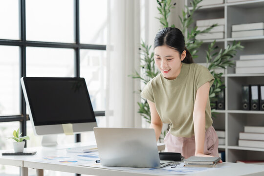 Focused Entrepreneur: A young woman diligently works on her laptop in a bright, modern office space, surrounded by stationery and plants, embodying focus and productivity.