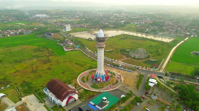 Aerial view of Menara Pandang Teratai surrounded by lush green fields and urban infrastructure in Purwokerto, Jawa Tengah, Indonesia.