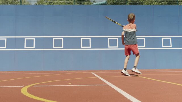 Slow motion. 7-year-old boy training his tennis skills against a practice wall