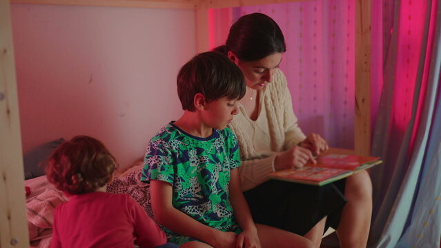 Mother reading bedtime story with son while toddler remains nearby creating nurturing family atmosphere focused on literacy learning and sibling presence in everyday home life