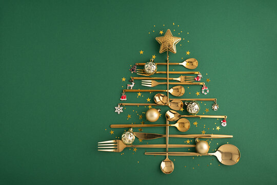 Golden cutlery arranged as a festive Christmas tree with ornaments and star on green background holiday concept