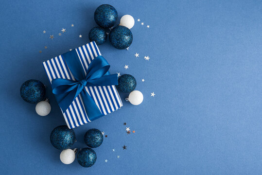 Elegant blue and white gift box with shimmering ornaments and scattered stars on a plain blue background