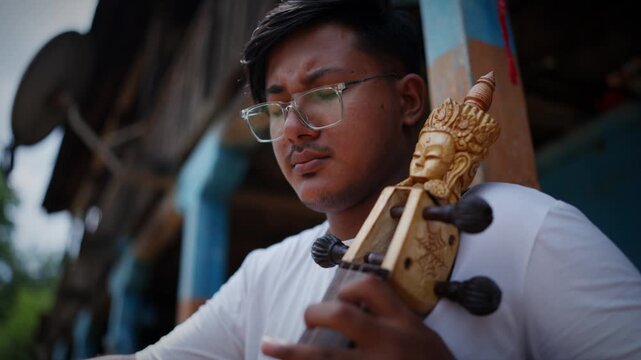 Close up of ornate carved tuning pegs on a sarangi with a musician softly blurred in the background beneath a traditional wooden porch