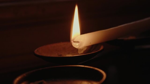 Close up of wax drops melting from burning church candle with bright flame glowing against dark atmospheric background