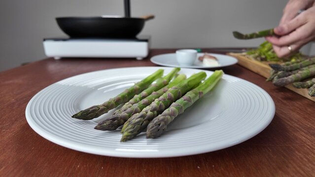 Close up view of fresh green asparagus spears arranged on a plain white plate, suggesting healthy eating or gourmet meal preparation for a spring brunch
