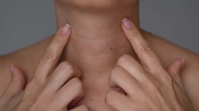 Young woman touching neck skin with visible lines and folds, aging skincare and beauty care concept on gray background