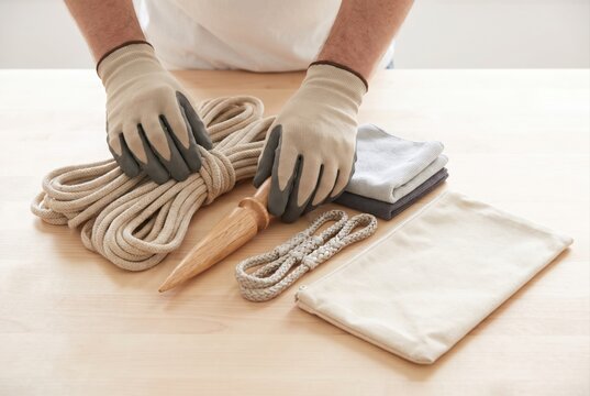 Hands wearing safety gloves holding a wooden splicing fid and a coil of rope