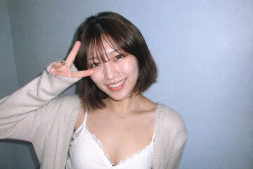 Fototapeta premium 室内の壁を背景に白いキャミソールの女性がピースサインをする、ピースサインの場面