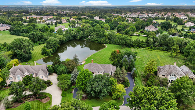 Tree-filled suburban neighborhood surrounding a landscaped pond in summer aerial view