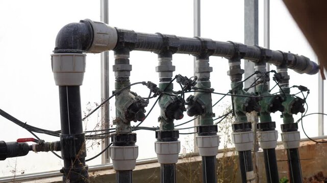 Close-up of irrigation pipes and control valves inside greenhouse agricultural system, reveal past foreground