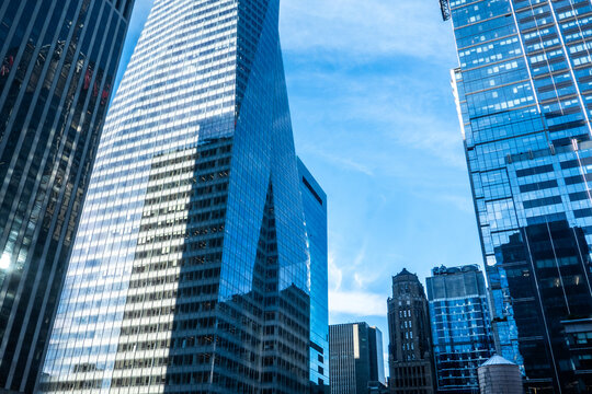Modern glass skyscrapers rise against a clear blue sky, featuring reflective facades, geometric architecture, corporate offices, and a dynamic urban business district in a contemporary city.