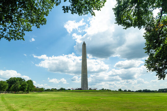 Washington Monument standing in a green park beneath dramatic clouds and blue summer sky, showcasing American history, iconic architecture, tourism, and a peaceful urban landscape.