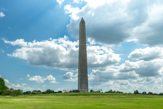Washington Monument standing in a green park beneath dramatic clouds and blue summer sky, showcasing American history, iconic architecture, tourism, and a peaceful urban landscape.