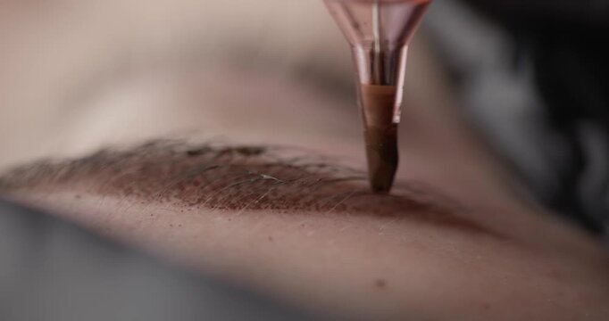 Slow motion microblading needle depositing pigment into eyebrow on face. Macro permanent makeup process.