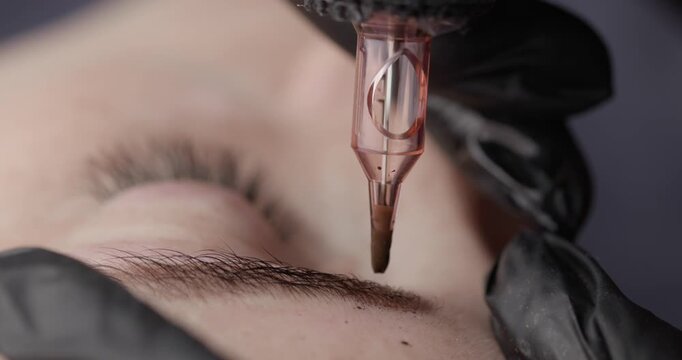 Macro permanent makeup process, technician applying microblading pigment to client's eyebrow in beauty studio.