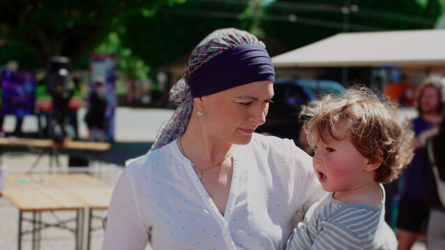 Mother holding toddler child during outdoor community gathering, affectionate parent child moment highlighting attachment, security, care and family connection