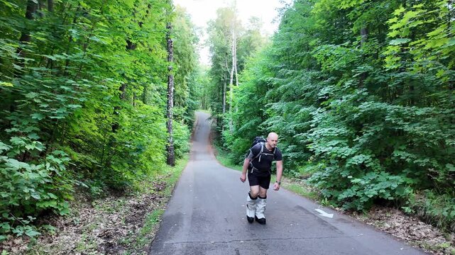 A determined man hikes up a lush forest path, training hard while carrying a heavy backpack. His climbing boots grip the ground as he pushes forward, focused and strong.