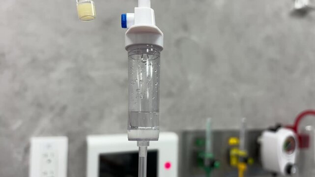 Close-up of an IV drip chamber dripping liquid saline solution in a hospital room, medical clinic, or ICU setting