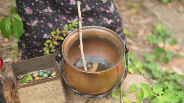 child hand stirring copper cauldron with stick, natural ingredients, water with leaves and berries inside, Halloween or fantasy witch crafting setup, Esoteric practice herbal medicine and magic potion