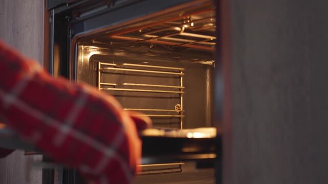 Taking baked dough sheet out of oven on parchment paper, with hands using an oven mitt and baking tray