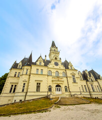 Obraz premium Castle stands tall under a blue sky. A large castle with pointed towers is seen in a clear blue sky. Grass is in front of the castle.
