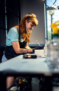 Side view of professional female tattoo artist sitting in her studio, using a stylus and graphics tablet to refine a final custom design for a client.